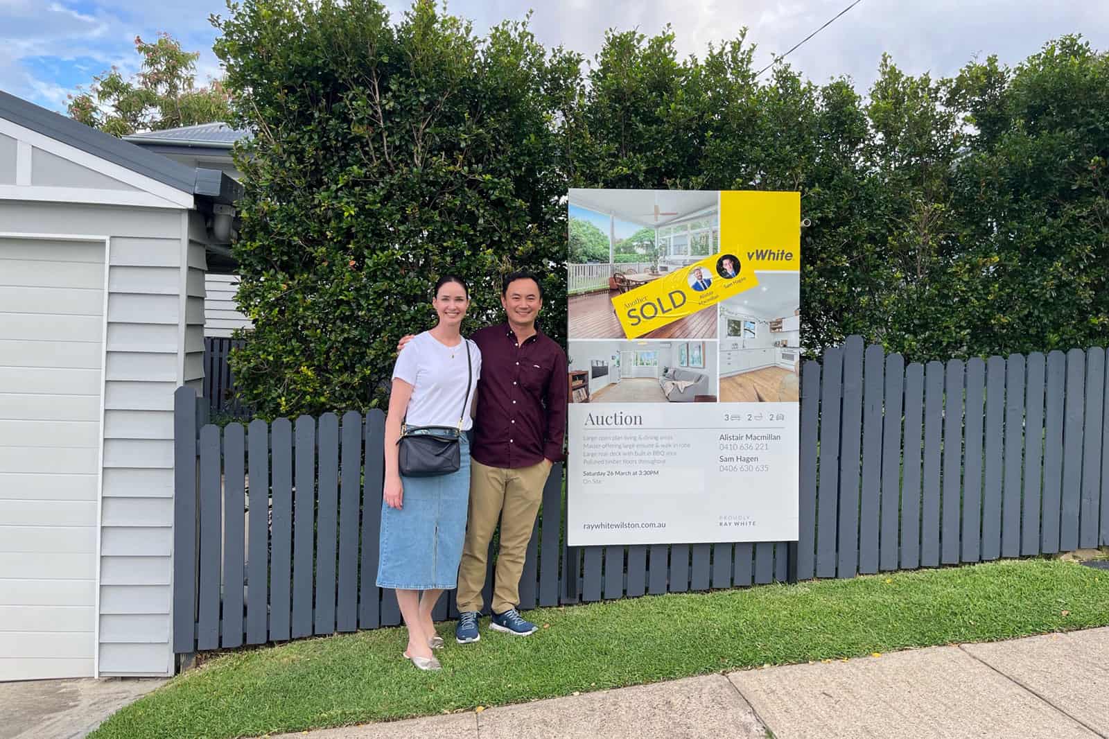 Happy couple standing next to a "sold" banner after winning an auction