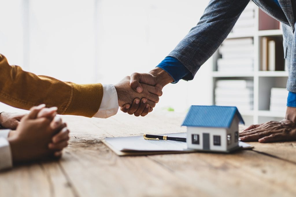 Real estate deal handshake over a model house on a desk